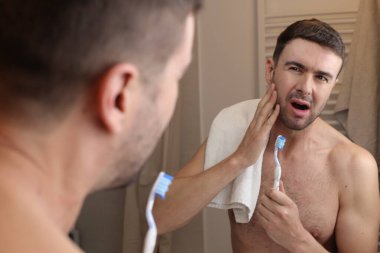 Banyoda aynanın önünde diş fırçası ve havluyla yakışıklı genç bir adamın portresi.