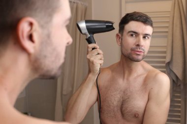 Yakışıklı genç adamın portresi banyoda aynanın önünde saçını kurutuyor.