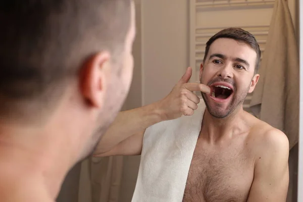 浴室の鏡の前で歯をチェックするハンサムな若い男の肖像画 — ストック写真