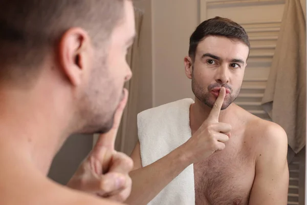 浴室の鏡の前で沈黙のジェスチャーを示すハンサムな若い男の肖像画 — ストック写真