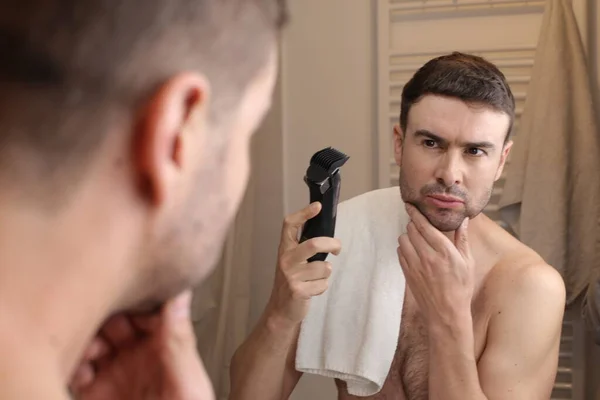 浴室の鏡の前に電気トリマーを持つハンサムな若い男の肖像画 — ストック写真