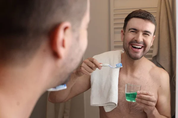 年轻英俊男子的肖像 在浴室的镜子前拿着牙刷和毛巾 — 图库照片