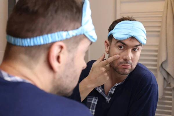 portrait of handsome young man with pajamas and sleeping eye mask in front of mirror in bathroom