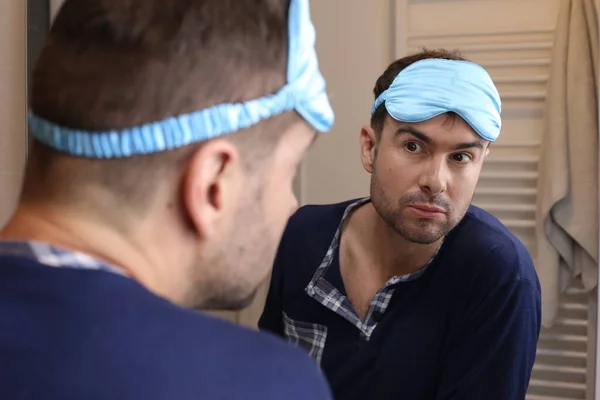 portrait of handsome young man with pajamas and sleeping eye mask in front of mirror in bathroom