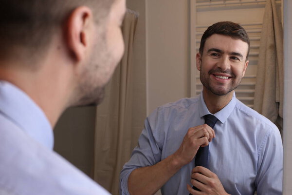 portrait of handsome young man with shirt and tie in front of mirror in bathroom
