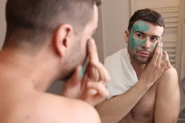 Porträtt Stilig Ung Man Tillämpa Grön Ansiktskräm Framför Spegeln Badrummet — Stockfoto