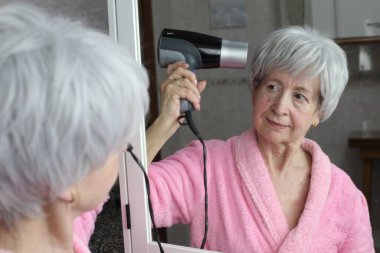 Banyoda aynanın önünde saç kurutma makinesi olan olgun bir kadının yakın plan portresi.