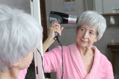 Banyoda aynanın önünde saç kurutma makinesi olan olgun bir kadının yakın plan portresi.