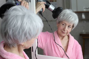 Banyoda aynanın önünde saç kurutma makinesi olan olgun bir kadının yakın plan portresi.