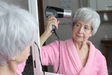 Banyoda aynanın önünde saç kurutma makinesi olan olgun bir kadının yakın plan portresi.