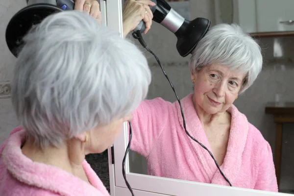 Banyoda aynanın önünde saç kurutma makinesi olan olgun bir kadının yakın plan portresi.
