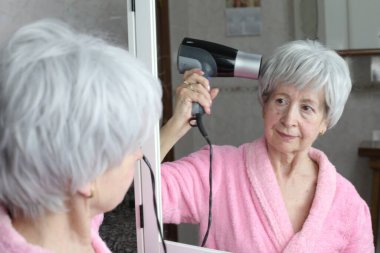 Banyoda aynanın önünde saç kurutma makinesi olan olgun bir kadının yakın plan portresi.