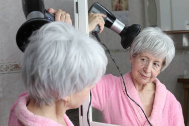 Banyoda aynanın önünde saç kurutma makinesi olan olgun bir kadının yakın plan portresi.