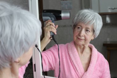 Banyoda aynanın önünde saç kurutma makinesi olan olgun bir kadının yakın plan portresi.