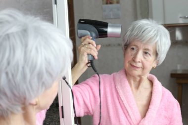 Banyoda aynanın önünde saç kurutma makinesi olan olgun bir kadının yakın plan portresi.