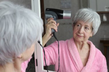 Banyoda aynanın önünde saç kurutma makinesi olan olgun bir kadının yakın plan portresi.