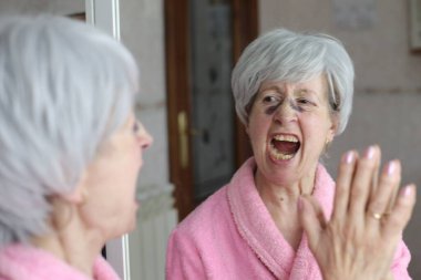 Banyoda aynanın önünde estetik ameliyat sonrası morlukları olan olgun bir kadının yakın plan portresi.