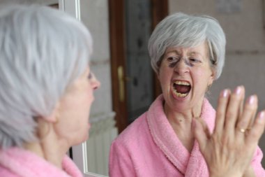 Banyoda aynanın önünde estetik ameliyat sonrası morlukları olan olgun bir kadının yakın plan portresi.