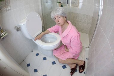 Banyoda tuvaletin yanında oturan yaşlı kadının geniş açı çekimi, gıda zehirlenmesi.