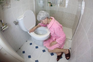Banyoda tuvaletin yanında oturan yaşlı kadının geniş açı çekimi, gıda zehirlenmesi.