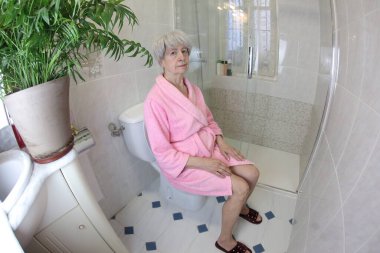 Yaşlı bir kadının tuvalette otururken geniş açılı görüntüsü.