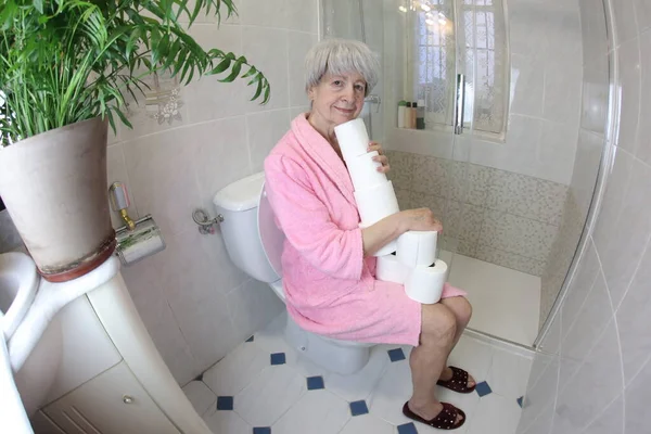 带卫生纸卷筒坐在马桶里的老年妇女广角镜头 — 图库照片