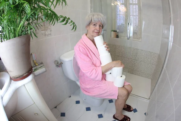 带卫生纸卷筒坐在马桶里的老年妇女广角镜头 — 图库照片