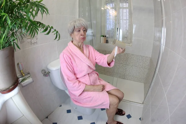 大角度拍摄的老年妇女与空厕纸辊坐在马桶里 — 图库照片