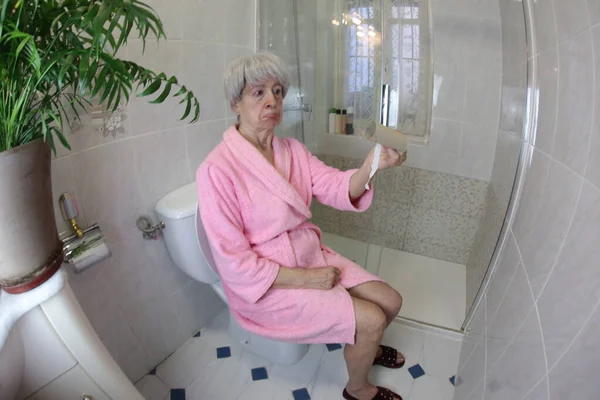 大角度拍摄的老年妇女与空厕纸辊坐在马桶里 — 图库照片