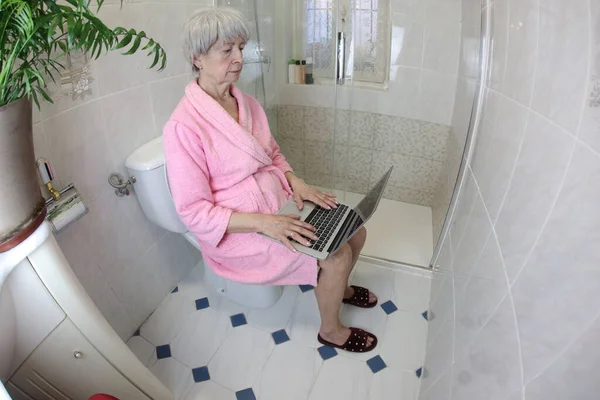 wide angle shot of senior woman working with laptop in toilet