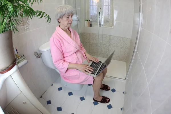 wide angle shot of senior woman working with laptop in toilet