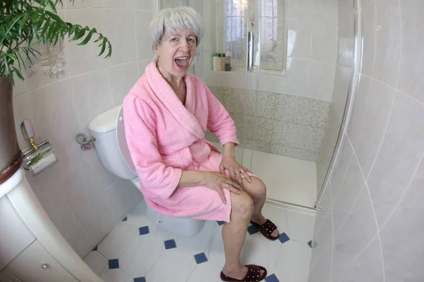 在浴室坐在马桶上的老年妇女尖叫的广角镜头 — 图库照片
