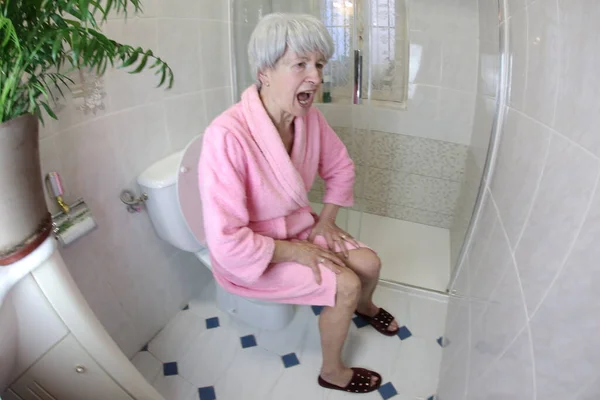 在浴室坐在马桶上的老年妇女尖叫的广角镜头 — 图库照片
