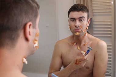 Banyoda aynanın önünde tıraş olurken kesikleri olan yakışıklı bir gencin portresi.