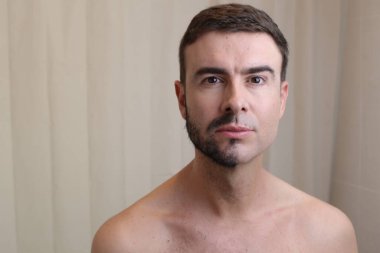 Yarı tıraşlı sakallı yakışıklı genç bir adam, kameraya bakıyor.