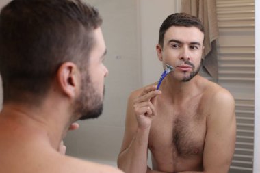 Banyoda aynanın önünde yarı tıraşlı sakallı yakışıklı genç adamın portresi.