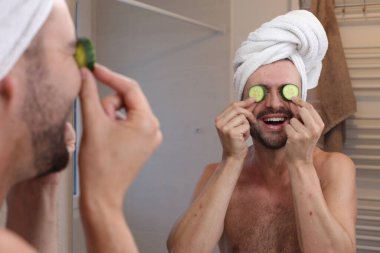 Kafasında havluyla genç bir adamın portresi ve banyoda aynanın önünde salatalıklar.