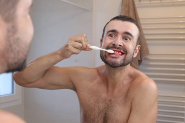 Kanayan diş etleri olan genç bir adamın portresi. Banyoda aynanın önünde dişlerini fırçalıyor.