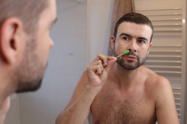 Banyoda aynanın önünde burun kıllarını ağdalayan genç adamın portresi.