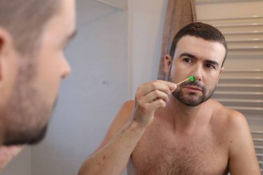 Banyoda aynanın önünde burun kıllarını ağdalayan genç adamın portresi.