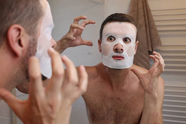 Stock image portrait of young man with skin mask in front of mirror in bathroom