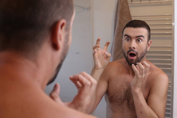 portrait of shocked emotional young man in front of mirror in bathroom