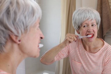 Banyoda aynanın önünde dişlerini fırçalarken dişleri kanayan olgun bir kadının yakın plan portresi.