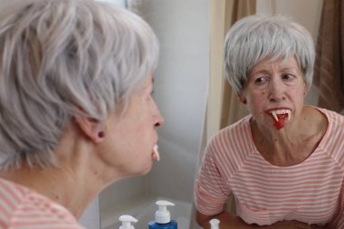 Tuvalette aynanın önünde vampir dişleri olan olgun bir kadının yakın plan portresi.