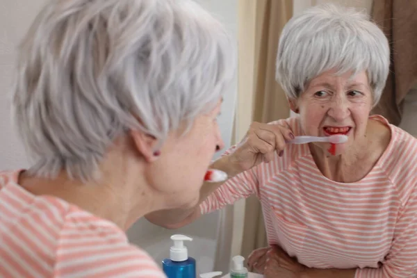 浴室で鏡の前で歯をブラッシングしながら歯茎を出血させている熟女のクローズアップ肖像画 — ストック写真