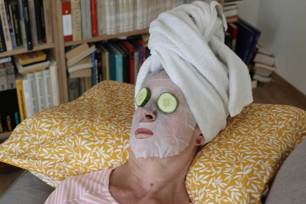 stock image close-up portrait of mature woman relaxing with towel on head, facial mask and cucumbers on eyes