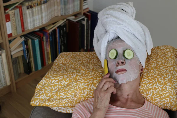 stock image close-up portrait of mature woman relaxing with towel on head, facial mask and cucumbers on eyes