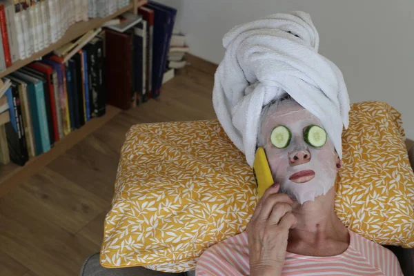 stock image close-up portrait of mature woman relaxing with towel on head, facial mask and cucumbers on eyes