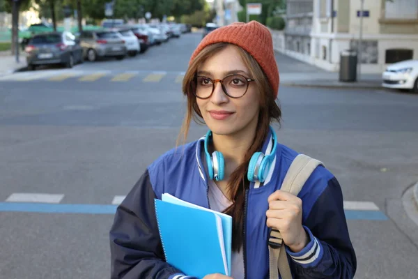 ビーニー帽子と眼鏡をかぶった学生女性が屋外を歩くノートを保持 — ストック写真