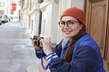 Şık hippi elbiseli, klasik kulaklıklı ve şehir caddesinde film kamerası olan güzel bir kadının portresi.